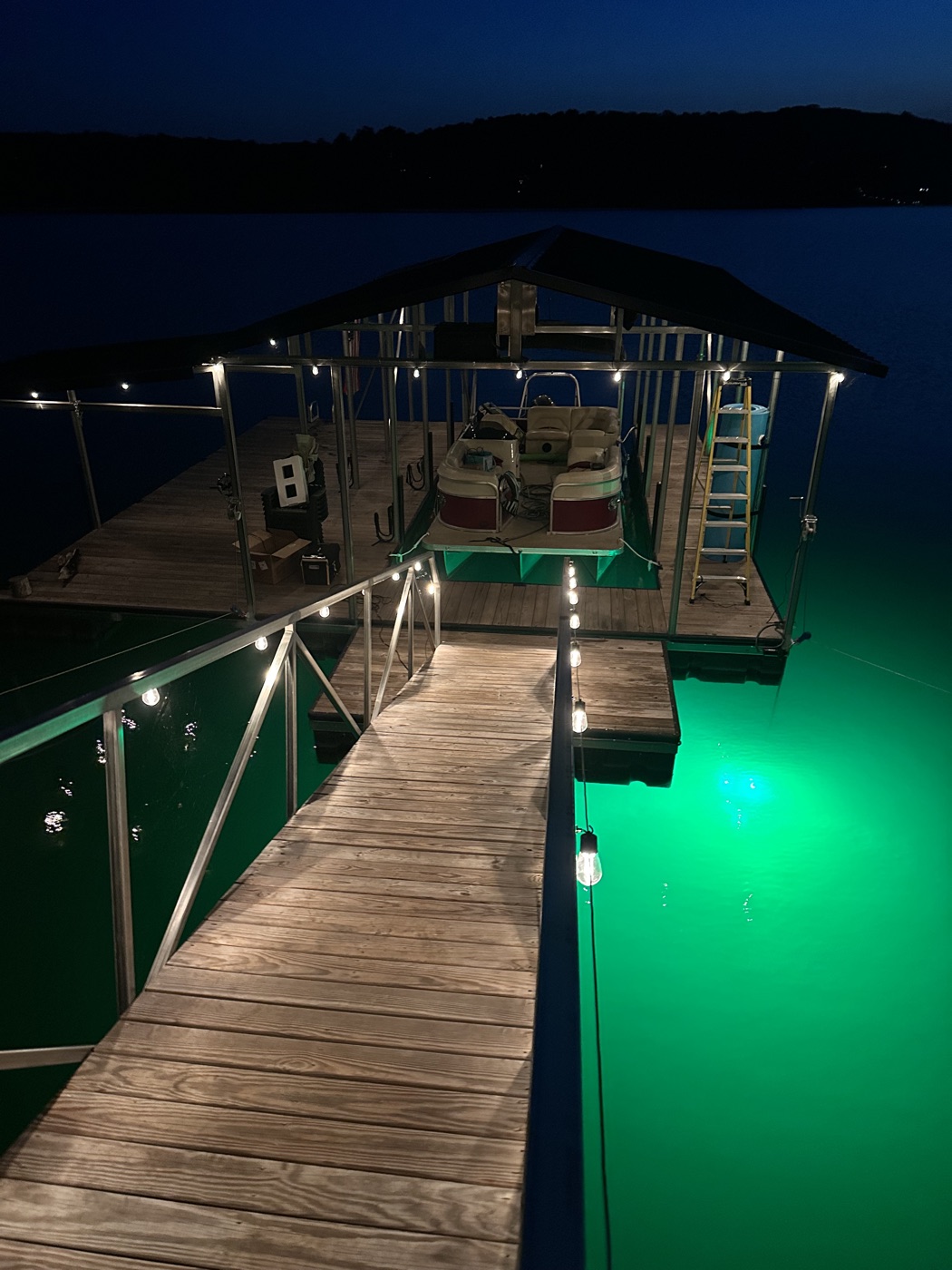 Boat dock on Smith Lake at night with string lights along the walkway and a green underwater fishing light, all running on solar power