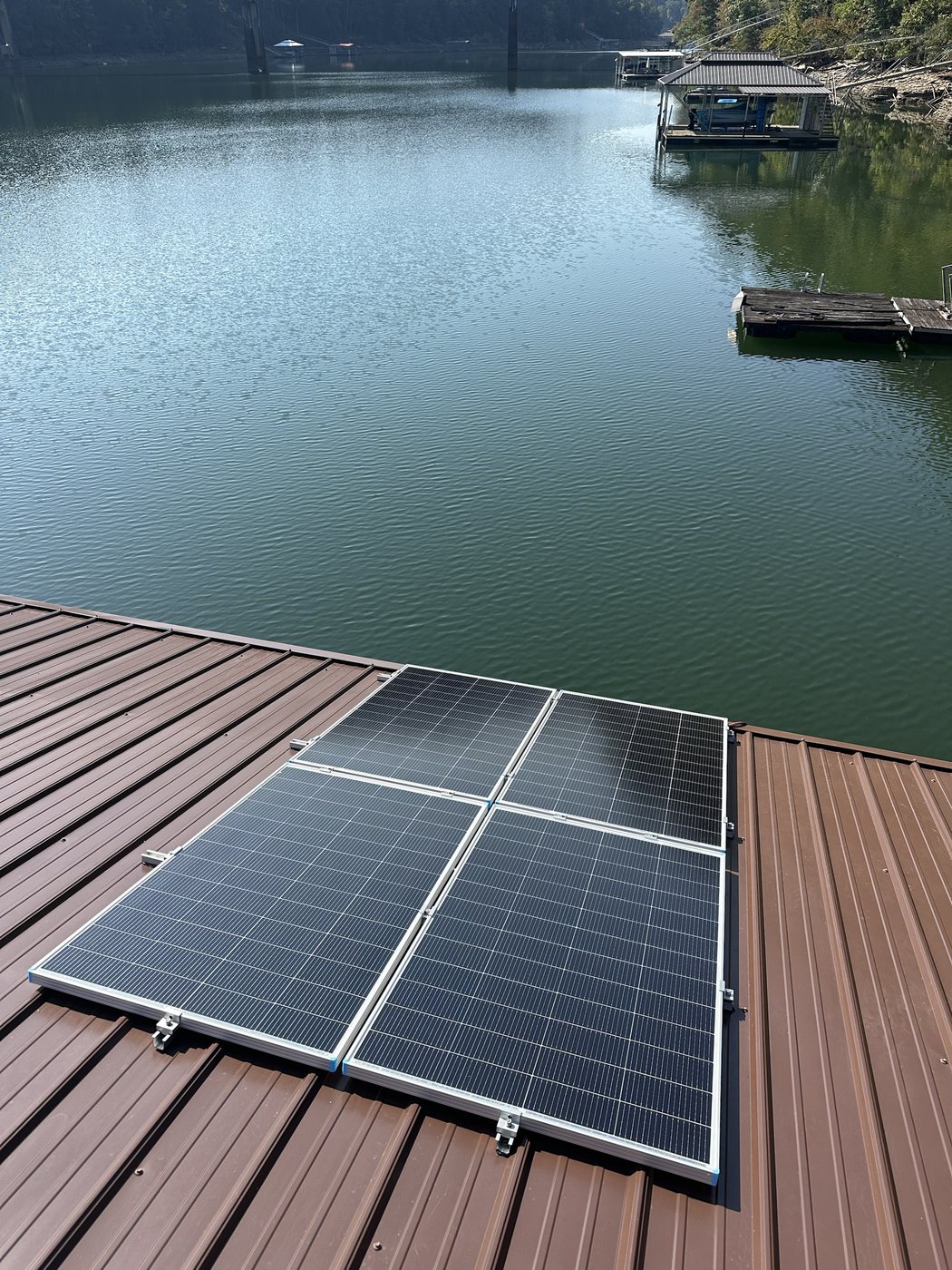Four solar panels mounted on a brown metal dock roof over Smith Lake, Alabama, with the lake and neighboring docks behind