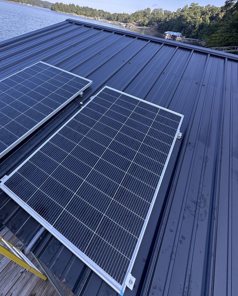 Two solar panels mounted on a dark metal dock roof on Smith Lake, Alabama, with the far shore behind